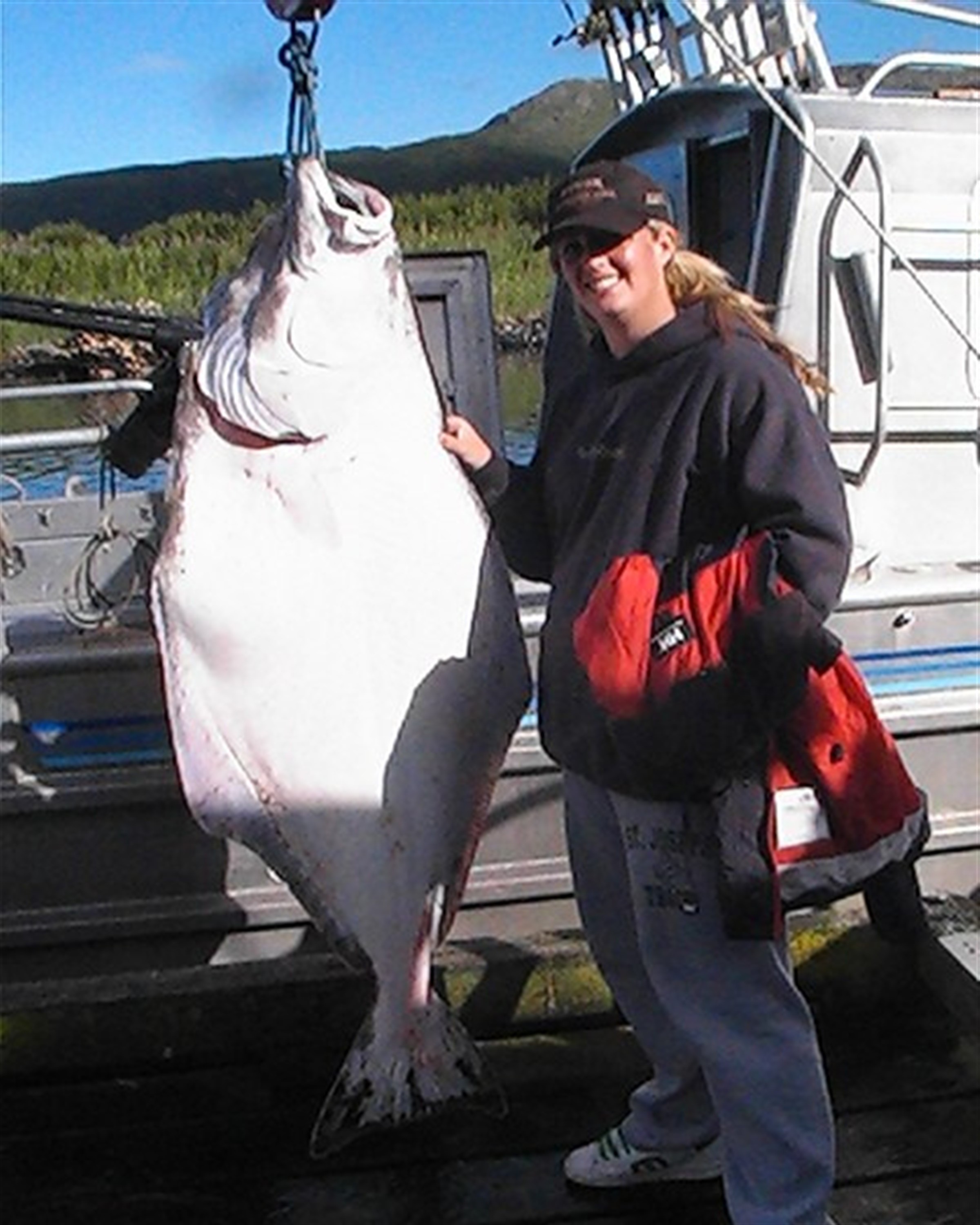 girl standing next to a caught halibut fish on a boat in Alaska